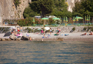 Strandbillede ved Camping Village Mare Pineta med gæster, parasoller og klipper i Friuli-Venezia Giulia, Italien.