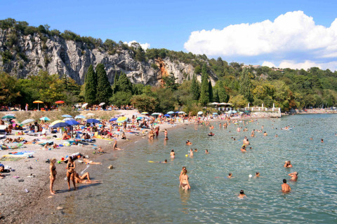 Personas disfrutan un día soleado en la playa de Camping Village Mare Pineta, con acantilados y vegetación detrás.