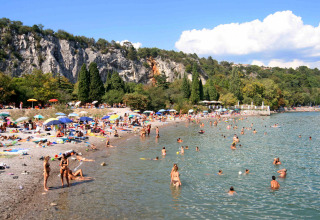 People enjoy a sunny day at the beach of Camping Village Mare Pineta, with cliffs and greenery in the background.