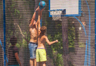 Ragazzi giocano a basket su un campo all'aperto recintato al Camping Village Mare Pineta, Friuli-Venezia Giulia.