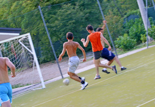Ragazzi giocano a calcio su un campo all’aperto immerso nel verde al Camping Village Mare Pineta, Italia.