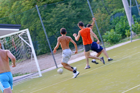 Jóvenes juegan al fútbol en un campo exterior rodeado de naturaleza en Camping Village Mare Pineta, Italia.