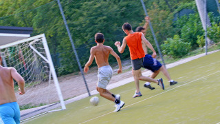 Jóvenes juegan al fútbol en un campo exterior rodeado de naturaleza en Camping Village Mare Pineta, Italia.