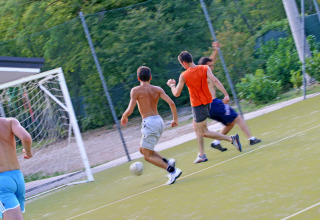 Young men play soccer on an outdoor field surrounded by greenery at Camping Village Mare Pineta, Italy.