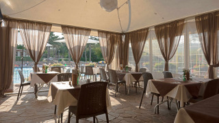 Zona de comedor con mesas y sillas frente a la piscina en Camping Village Mare Pineta, Friuli-Venezia Giulia.