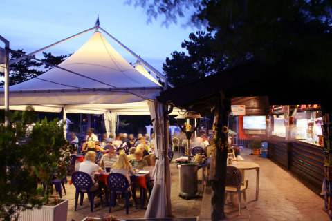 Cena all'aperto sotto tenda al Camping Village Mare Pineta, Friuli-Venezia Giulia, Italia al tramonto.