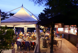 Udendørs spisested under telt på Camping Village Mare Pineta, Friuli-Venezia Giulia, Italien ved skumringen.