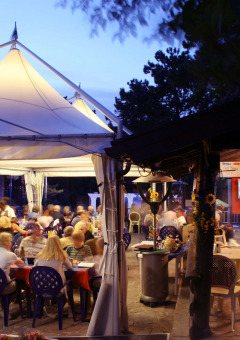 Cena al aire libre bajo carpa en Camping Village Mare Pineta, Friuli-Venezia Giulia, Italia al atardecer.