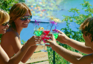 Trois amis trinquent avec des cocktails colorés en plein air au soleil au Camping Village Mare Pineta, Italie.