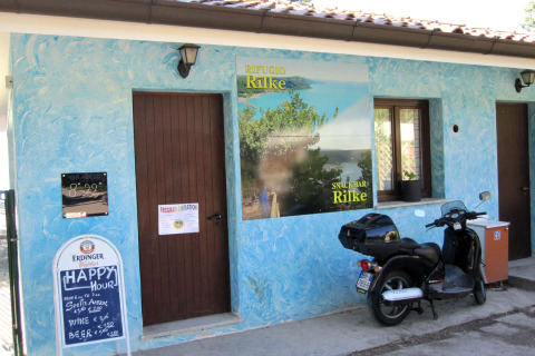 Entrada del Snack Bar Rilke en Camping Village Mare Pineta en Italia, con una scooter y paredes azules.