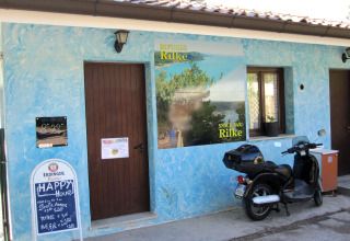 Entrance of Snack Bar Rilke at Camping Village Mare Pineta, Italy, with a scooter and blue textured walls.