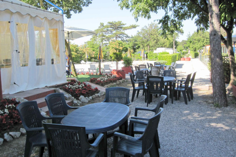 Outdoor dining area with plastic tables and chairs at Camping Village Mare Pineta, Friuli-Venezia Giulia, Italy.
