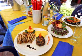 Table extérieure avec plats italiens, poisson, salade et boissons au Camping Village Mare Pineta, Friuli-Venezia Giulia.