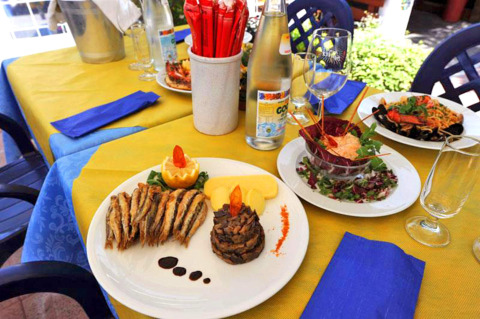 Table extérieure avec plats italiens, poisson, salade et boissons au Camping Village Mare Pineta, Friuli-Venezia Giulia.