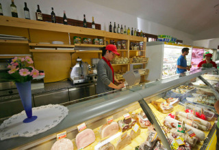 Binnenzicht van een winkel met verswaren en personeel, bij Camping Village Mare Pineta in Italië.