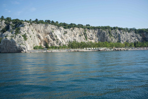 Vista del Camping Village Mare Pineta in Friuli-Venezia Giulia, Italia, con scogliere, alberi e mare blu.