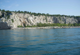 Vue du Camping Village Mare Pineta en Frioul-Vénétie Julienne, Italie, avec falaises, arbres et mer bleue.