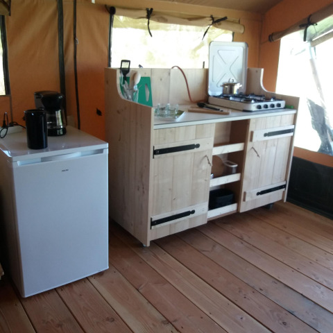 Pequeña cocina en una cabaña con mini nevera, cafetera y cocina de gas sobre suelo de madera.