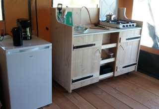 Pequeña cocina en una cabaña con mini nevera, cafetera y cocina de gas sobre suelo de madera.