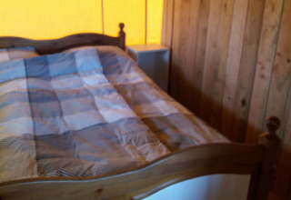 Dormitorio acogedor de lodge con paredes de madera, cama de madera y colcha a cuadros bajo luz cálida.