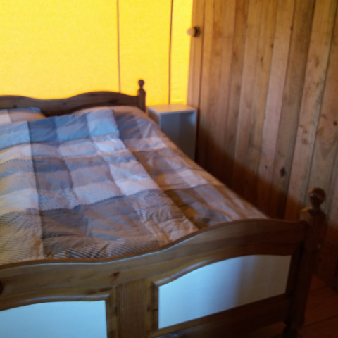 Camera da letto di una lodge, pareti in legno, letto in legno e copriletto a quadri sotto luce calda.