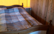 Sfeervolle lodge slaapkamer met houten wanden, houten bed en geruite deken in warm geel licht.