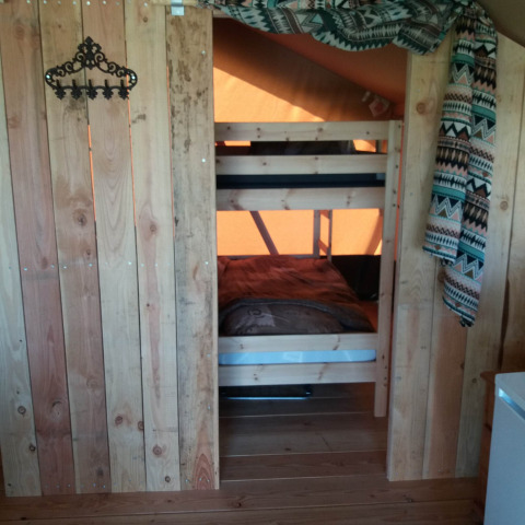 Interno accogliente di un lodge con letto a castello in legno, pareti rustiche e tenda decorativa sopra.