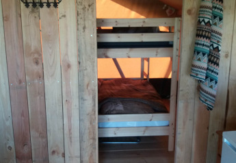 Intérieur chaleureux d’un lodge avec lits superposés en bois, murs rustiques et tissu à motifs au-dessus.