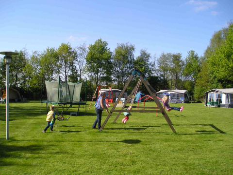 Niños juegan en el parque infantil junto a la tienda Stoere Safari en Camping de Berghoeve, Países Bajos, césped verde.