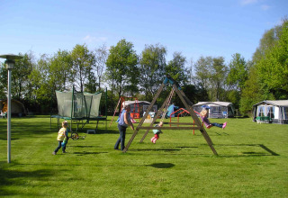 Niños juegan en el parque infantil junto a la tienda Stoere Safari en Camping de Berghoeve, Países Bajos, césped verde.