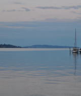Vista di un lago tranquillo con barche a vela ormeggiate vicino a un glamping al crepuscolo.
