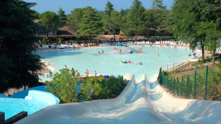 Gran piscina con toboganes de agua y personas, rodeada de árboles en Altomincio Family Park, Lombardía.