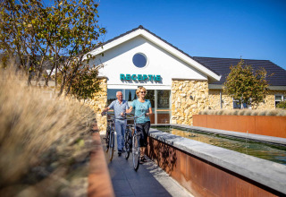 Deux personnes avec des vélos devant la réception du Resort Mooi Bemelen à Limbourg, Pays-Bas, un jour ensoleillé.