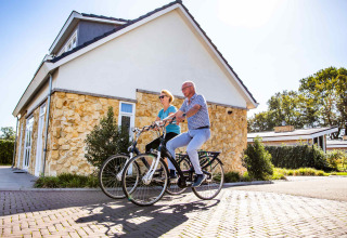 Un couple âgé fait du vélo devant un cottage en pierre au Resort Mooi Bemelen, Limburg, Pays-Bas, en été.