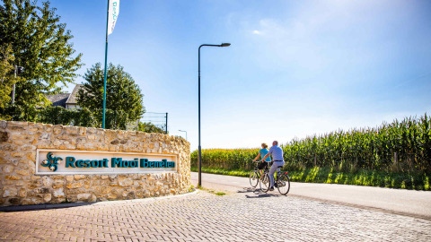 Zwei Personen fahren Fahrrad am Eingang des Resort Mooi Bemelen vorbei, umgeben von Feldern in Limburg.