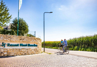 To personer cykler forbi indgangen til Resort Mooi Bemelen, omgivet af majsmarker i Limburg, Holland.