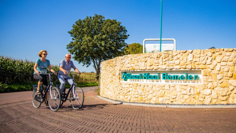 Dos personas montan en bicicleta junto a la entrada del Resort Mooi Bemelen, un parque vacacional en Limburg, Países Bajos.