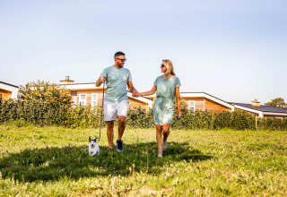 Couple marchant avec un chien à Resort Mooi Bemelen, parc de vacances à Limbourg, Pays-Bas, journée ensoleillée.