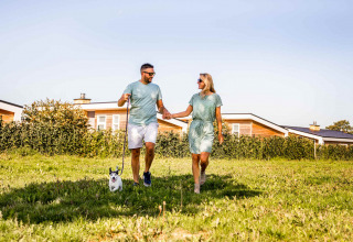 Coppia che passeggia con cane al Resort Mooi Bemelen, parco vacanze in Limburg, Paesi Bassi, giornata di sole.