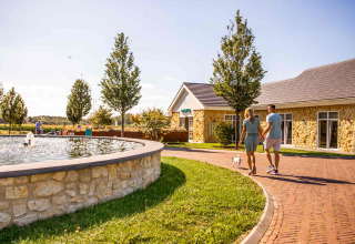 Coppia che cammina con un cane vicino a una fontana al Resort Mooi Bemelen, villaggio vacanze in Limburgo, Paesi Bassi.