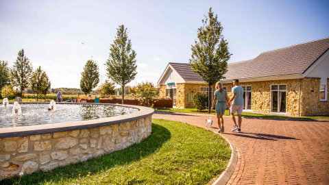 Couple walking hand in hand with a dog by a fountain at Resort Mooi Bemelen holiday park in Limburg, Netherlands.