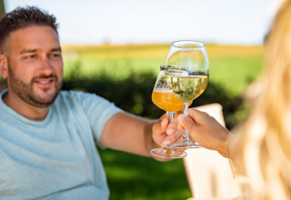 Two people clinking wine and beer glasses outdoors at Resort Mooi Bemelen, a holiday park in Limburg, Netherlands.