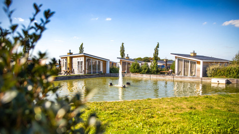 Cabañas vacacionales junto a un estanque con fuente en Resort Mooi Bemelen, Limburgo, Países Bajos, de día soleado.