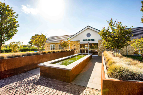 Eingang des Resort Mooi Bemelen in Limburg, Niederlande mit Rezeption, Springbrunnen und Gartenlandschaft.