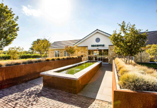 Toegang tot Resort Mooi Bemelen in Limburg, Nederland, met receptie, fontein en groene omgeving.