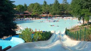Parc aquatique dans un lodge avec piscine, toboggans, chaises longues et arbres par une journée ensoleillée.