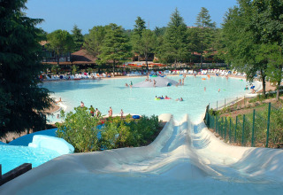 Waterpark bij een lodge met zwembad, glijbanen, ligstoelen en veel bomen op een zonnige dag.