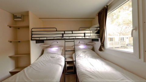 Habitación glamping con dos camas individuales, litera superior, estanterías y ventana grande, ambiente acogedor.