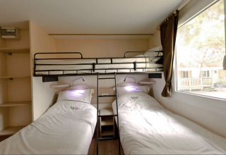 Habitación glamping con dos camas individuales, litera superior, estanterías y ventana grande, ambiente acogedor.