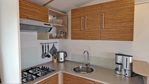 Cocina moderna en alojamiento glamping, con estufa, fregadero, hervidor y cafetera en la encimera.